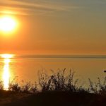 Летний рассвет над морем. Солнце, солнечная дорожка на воде, одинокая лодка и оранжевые краски неба.